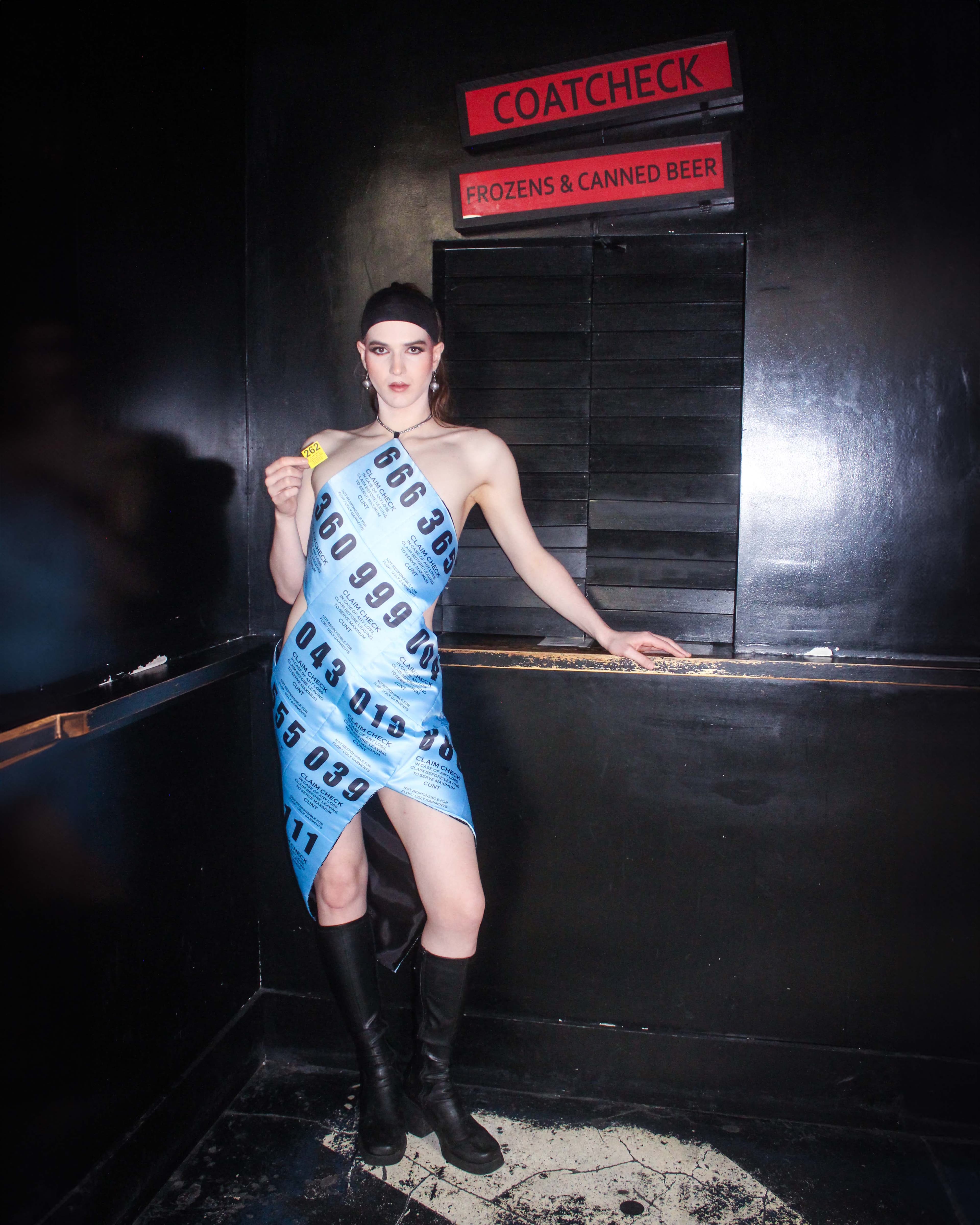 The blue, ticket-print Coat Check Dress, photographed beneath a coat check sign